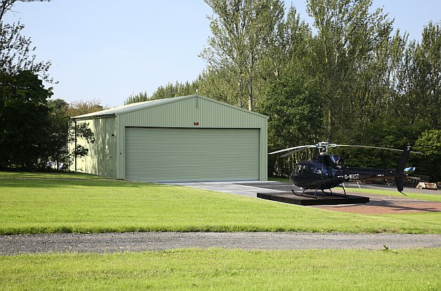 Green steel aircraft hangar with wide access doors in private setting.