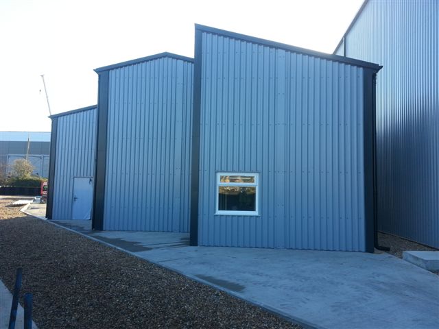 Grey prefabricated steel storage building with blue flashings and personnel access door and small window.