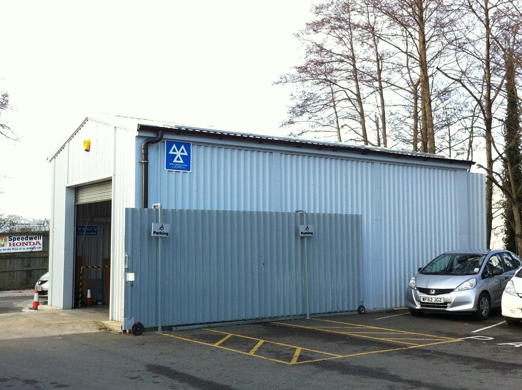 Side view of Speedwell Honda's steel MOT testing building with roller shutter entrance and secure gated compound. Solar Panelled roof.