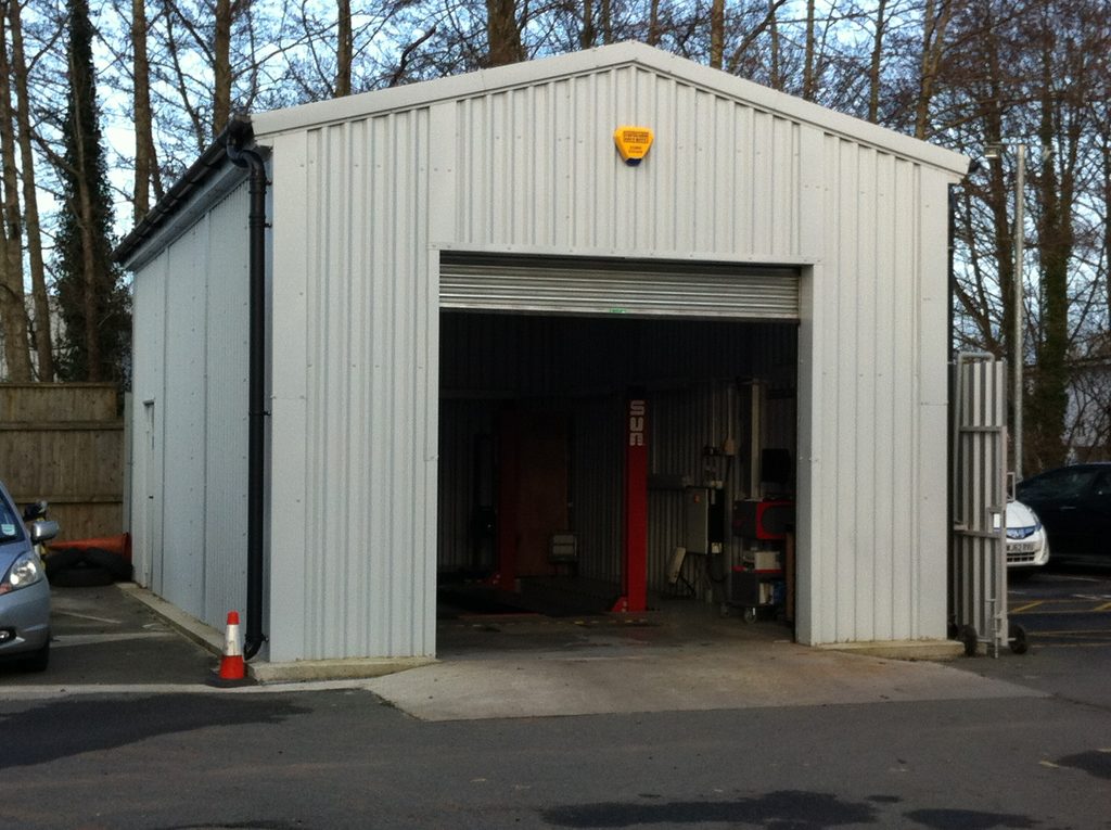 Prefabricated steel MOT testing building with large vehicle inspection bay entrance.