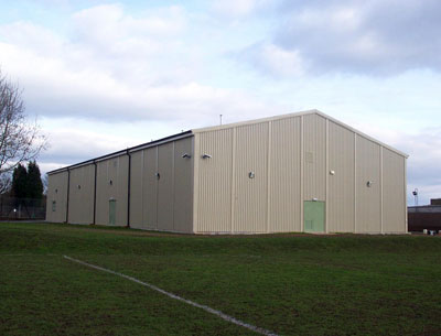 Large beige prefabricated steel gymnasium building with pitched roof.
