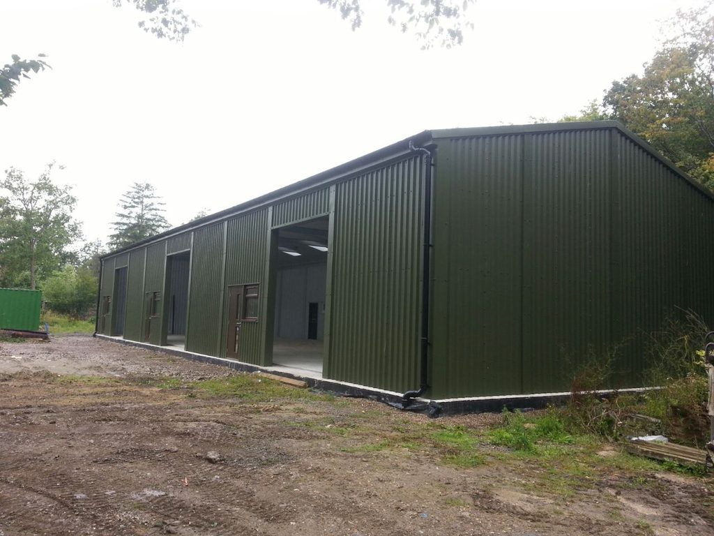 Prefabricated steel industrial building for Hemlon, finished in deep green cladding to blend in with the landscape with multiple large access openings and personnel doors and windows.