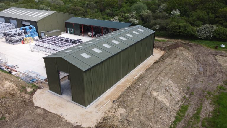 Aerial view of Utranazz steel storage building with dark green cladding, rooflights and large vehicle access opening in front gable elevation.