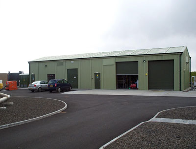 Light green steel wastewater treatment works building featuring multiple large equipment access doors and personnel entrances.