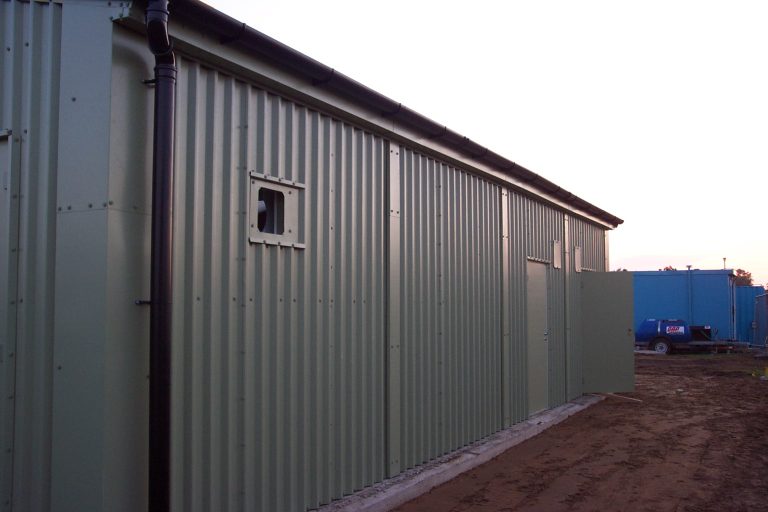 Side elevation of prefabricated steel wastewater treatment building with green cladding, small ventilation louvre and external wastewater pipework.