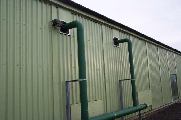 Close up of green steel wastewater treatment works building showing external pipework and connections through the cladding.