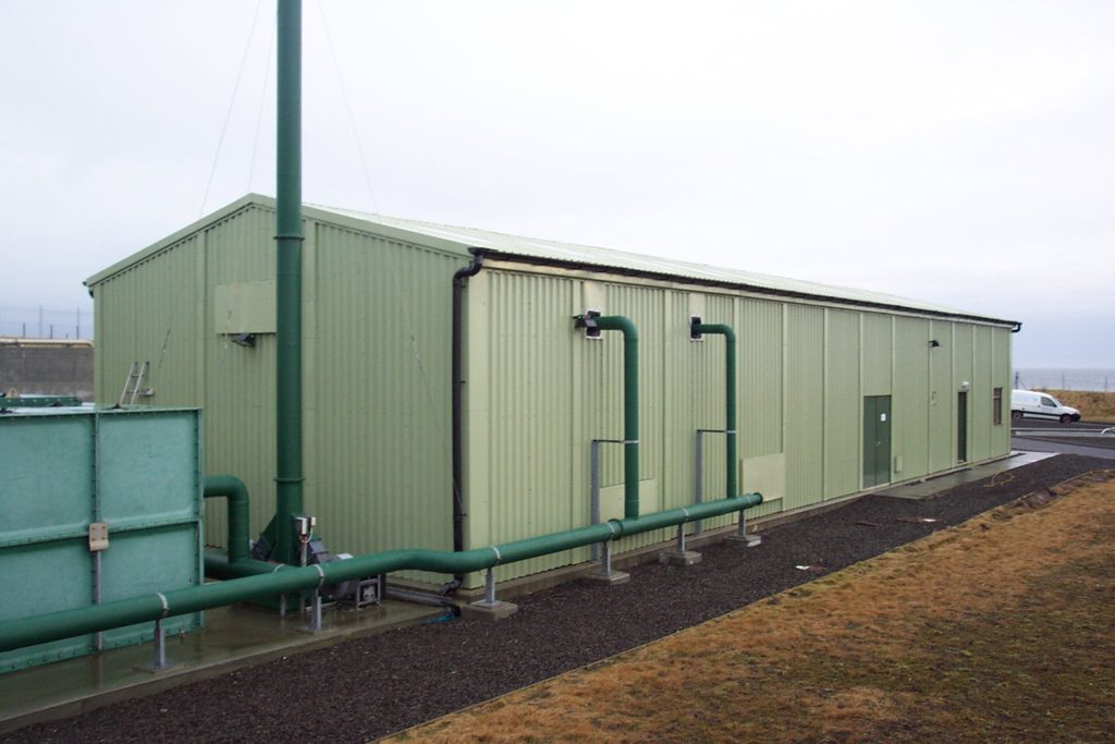 Green prefabricated steel building housing equipment at a wastewater treatment works.