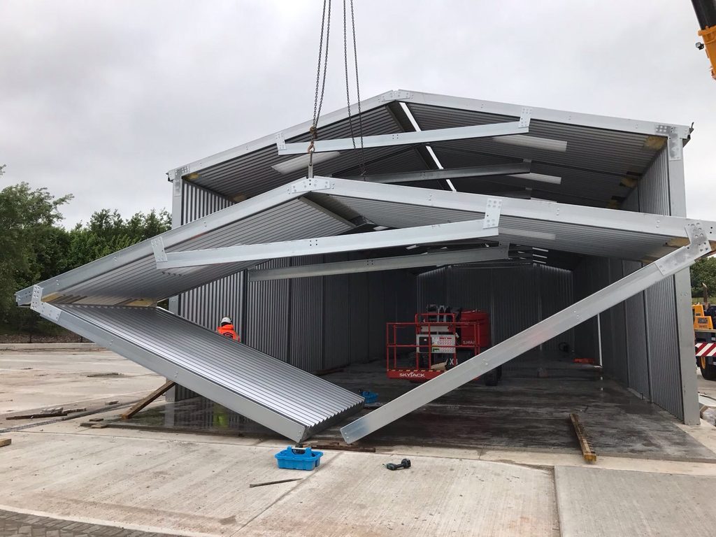 Prefabricated modular steel building section being lifted into position by a crane during installation.